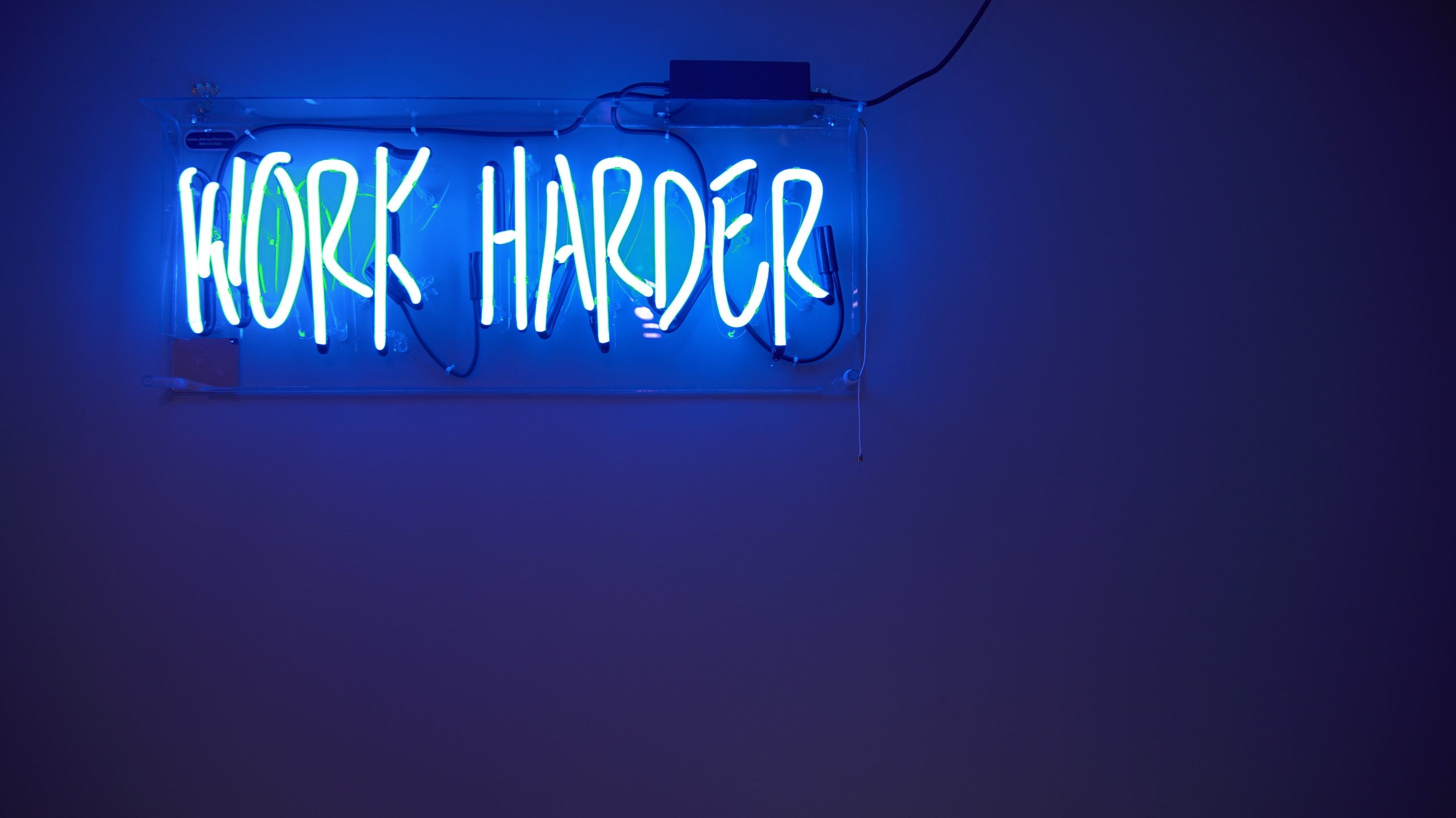 Leuchtschrift "Work harder" auf blauem Hintergrund